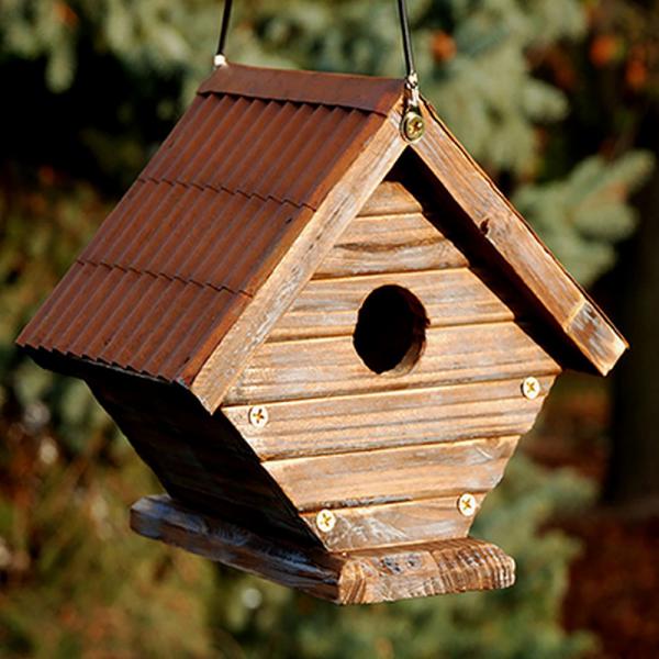 Rustic wooden wren house with corrugated metal roof hanging outdoors