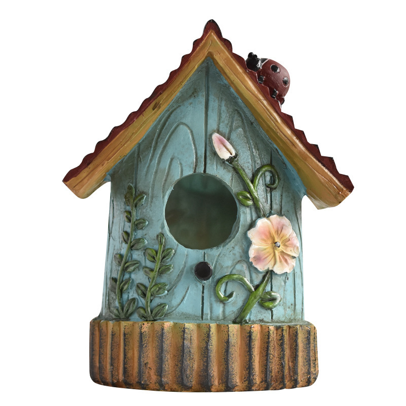 Rustic resin hanging birdhouse in turquoise with orange roof and leaf details hanging in a fig tree - view 3